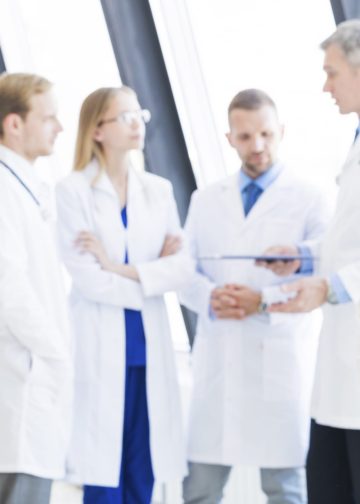 Successful female doctor and her team on background in clinical office