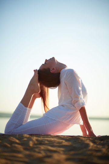 Yoga on beach Photo of active and fit girl doing stretching exercise against clear sky